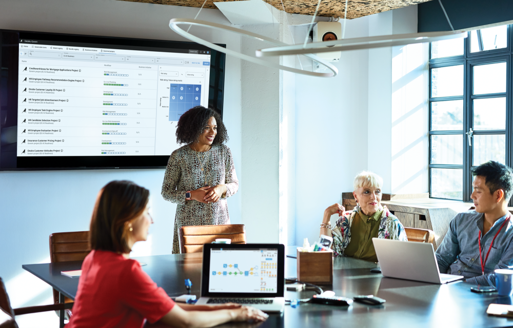 A group of people in a meeting room looking at a screen that shows Dataiku product to explain how to accelerate regulatory compliance for full AI portfolio